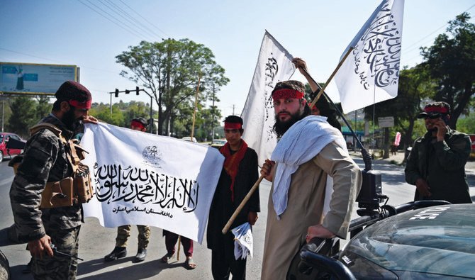 Taliban fighters waive flags while standing guard along a road in the Afghan capital Kabul on Thursday. Taliban banned protests due to security concerns. (AFP)