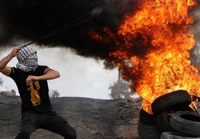 A Palestinian protester hurls rocks from behind burning tires during confrontations with Israeli security forces in the West Bank village of Beita on Sept. 24, 2021. (AFP)