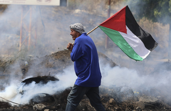 A Palestinian protester lifts a national flag amid confrontations with Israeli security forces in the occupied West Bank, on May 21, 2021. (File/AFP)