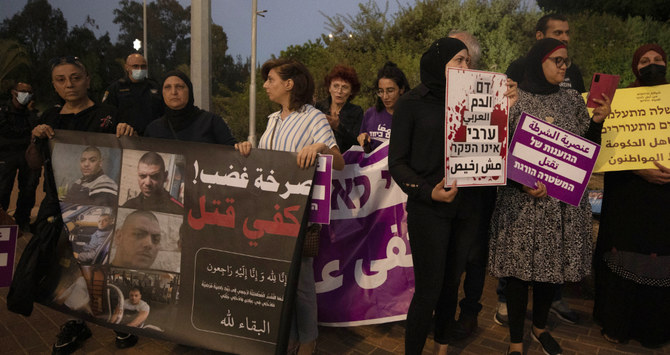Protesters hold signs and chant slogans during a demonstration against violence near the house of Public Security Minister Omer Barlev in the central Israeli town of Kokhav Ya'ir, Saturday, Sept. 25, 2021. (AP)