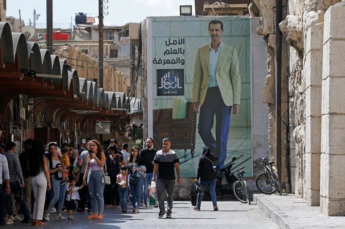 Syrians walk in front of a poster of President Bashar al-Assad near the Grand Umayyad Mosque in Damascus on September 23, 2021. (AFP)