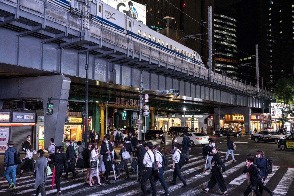 People cross a street while a Shinkansen leaves the city in Tokyo's Shimbashi area on October 1, 2021. (AFP)