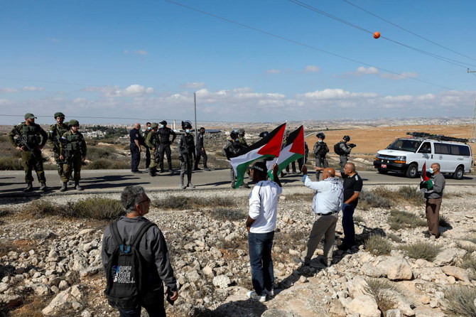 Demonstrators hold Palestinian flags as members of Israeli forces stand guard during a protest against Israeli settlements in Masafer Yatta, in the Israeli-occupied West Bank October 23, 2021. (Reuters)