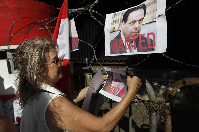 An activist hangs photos of former Lebanese prime minister Hassan Diab and former minister of public works Youssef Fenianos, who are both charged with negligence leading to deaths over the Beirut blast. (AP)