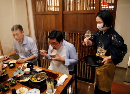 A waitress serves Japanese sake to customers during dinner at Japanese restaurant Kazu, on the first day after Japan lifted the state of emergency imposed due to the coronavirus disease (COVID-19) outbreak, in Tokyo, Japan, October 1, 2021. (Reuters)