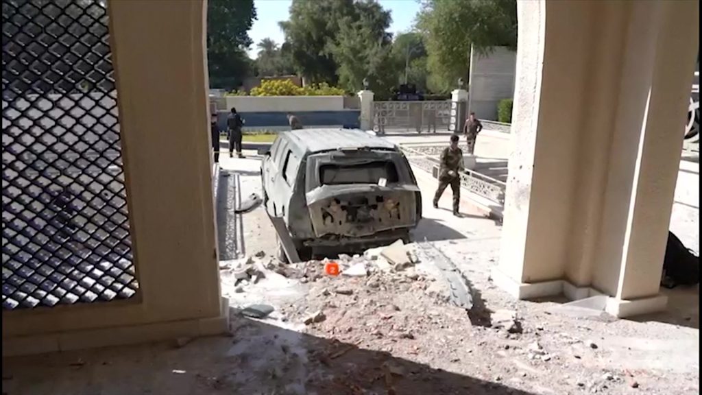This image grab taken from footage released by the Iraqi Prime Minister's press office on November 7, 2021 shows security forces near a damaged vehicle inspecting the aftermath of a drone strike on the prime minister's residence which took place earlier the same day. (AFP)
