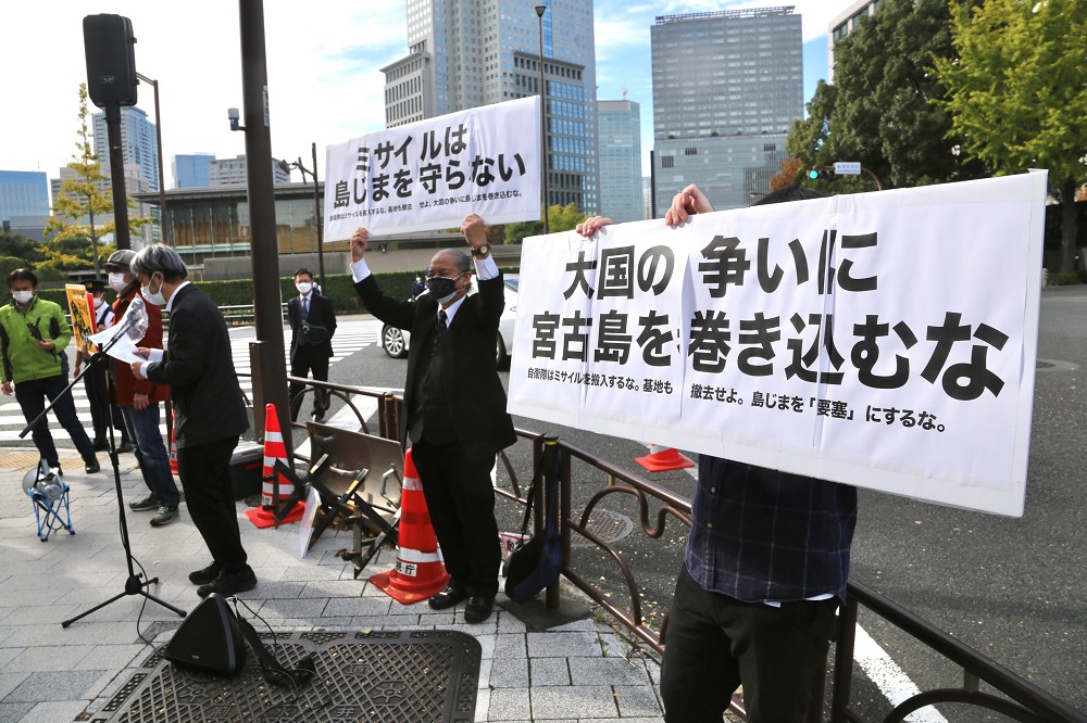 Protestors on the sidewalk facing the Prime Minister’s building in Tokyo, raising signboards that say, “Missiles don’t protect the island” and “Don't involve Miyakojima island in the battle between the big powers.” (ANJ/ Pierre Boutier)