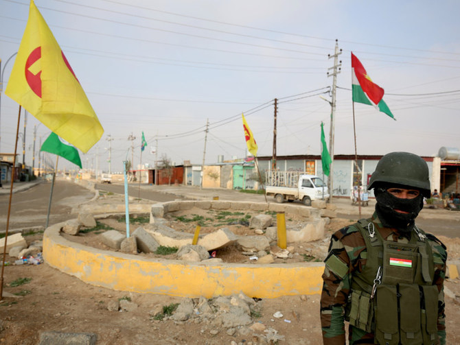 A Kurdish Peshmerga soldier of the Kurdish KDP party stands guard in front of KDP and PUK flags at a destroyed roundabout in the town of Snuny in northern Iraq. (AP)