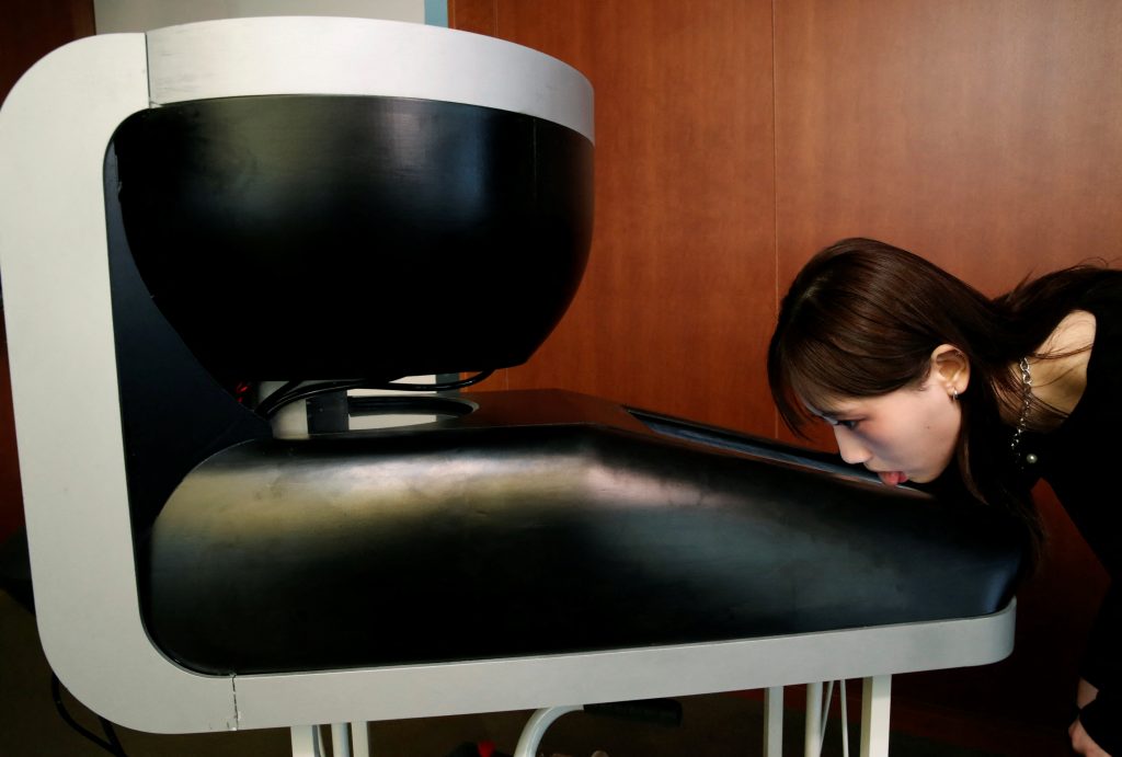 Student of Meiji University Yuki Hou licks a screen of Taste the TV (TTTV), a prototype lickable TV screen that can imitate the flavours of various foods, during its demonstration at the university in Tokyo, Japan, December 22, 2021. Picture taken on December 22, 2021. (Reuters)