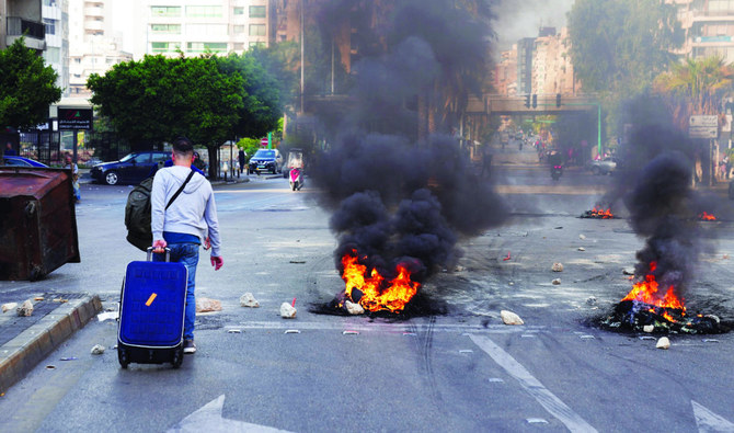 A man drags a suitcase as he walks along a road blocked with burning tires during a protest on the back of the continuing deterioration of living conditions, in Beirut. (Reuters)