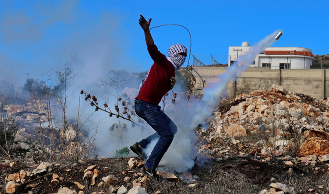 A Palestinian protester uses a slingshot to return a tear gas canister amid clashes with Israeli security forces in the village of Kfar Qaddum in the occupied West Bank on December 10, 2021. (AFP)