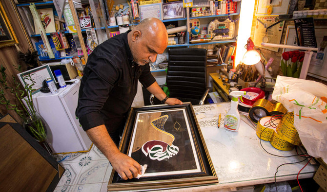 Iraqi calligrapher Wael al-Ramdan, 49, wipes the glass on one of his Arabic calligraphy framed art pieces at his workship in al-Ashar district of Iraq's southern city of Basra on December 19, 2021. (AFP)