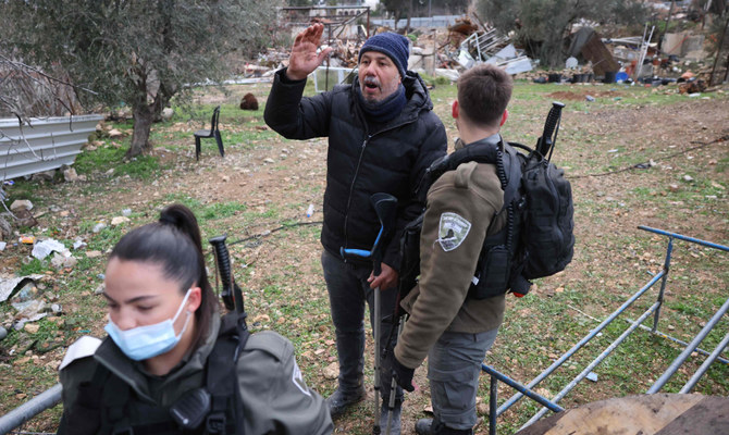 A member of the Israeli forces escorts a man on crutches, supporter of the Palestinian Salhiya family, away from the ruins of the demolished house, in Sheik Jarrah neighborhood on January 19, 2022. (AFP)