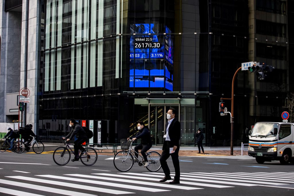 People cross a road near an electronic quotation board displaying closing numbers of the Nikkei 225 index of the Tokyo Stock Exchange in Tokyo on January 27, 2022. (