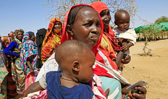 Displaced Sudanese women carry their children as they stand in queue as they wait for the arrival of the World Food Programme (WFP) trucks in the outskirts of Nyala town, South Darfur. (AFP)