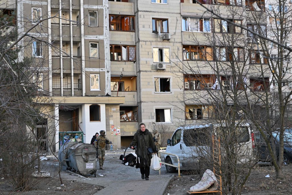 A woman carries belongings out of a damaged apartment block after it was hit by debris from a downed rocket in Kyiv on March 17, 2022, as Russian forces press in on the Ukrainian capital. (AFP)