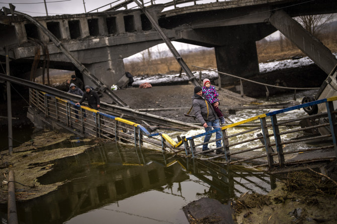 A militiaman carries a child as he helps a fleeing family across a damaged bridge on the outskirts of Kyiv, Ukraine. (AP)