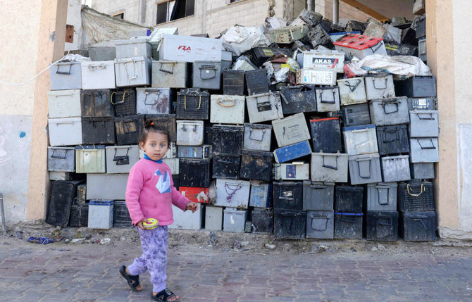 A Palestinian girl walks past a stack of discarded batteries slated for recycling in Khan Yunis in the southern Gaza Strip, on February 14, 2022. (AFP)