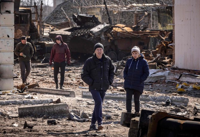 Residents walk amid rubble near a destroyed Russian tank in the northeastern city of Trostianets, on March 29, 2022. (AFP)