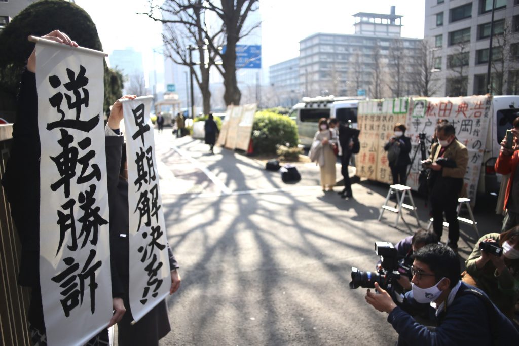 Japanese staff of the legal office display banners informing the public and media of the ruling on the case. Banners said “(the case) is a win in reversal”, and “early ruling”. (ANJP Photo)
