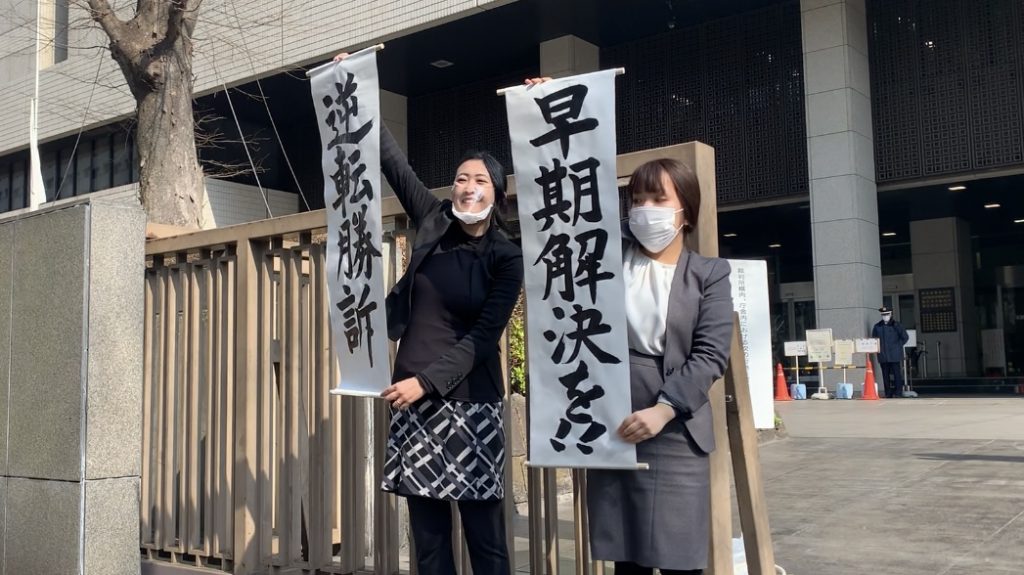 Japanese staff of the legal office display banners informing the public and media of the ruling on the case. Banners said “(the case) is a win in reversal”, and “early ruling”. (ANJP Photo)