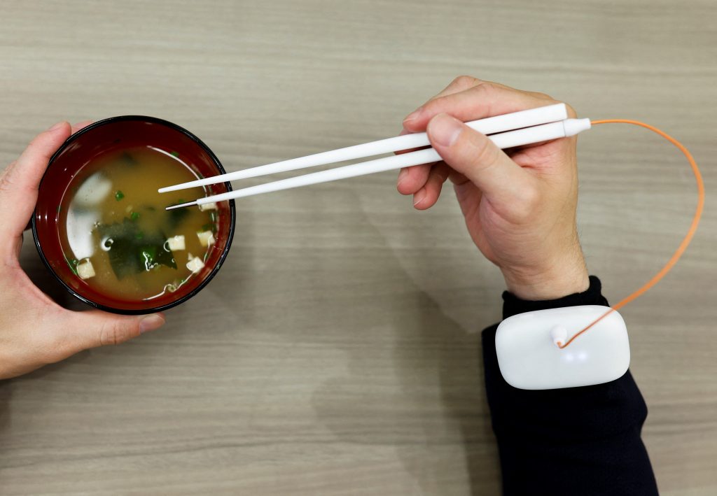 An employee of Kirin Holdings demonstrates chopsticks that can enhance food taste using an electrical stimulation waveform that was jointly developed by the company and Meiji University's School of Science and Technology Professor Homei Miyashita, in Tokyo, Japan April 15, 2022. Picture taken April 15, 2022. (REUTERS/Issei Kato)