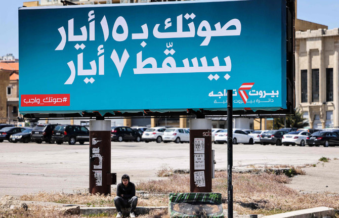 A youth sits underneath a giant billboard for the upcoming parliamentary election with text in Arabic reading 