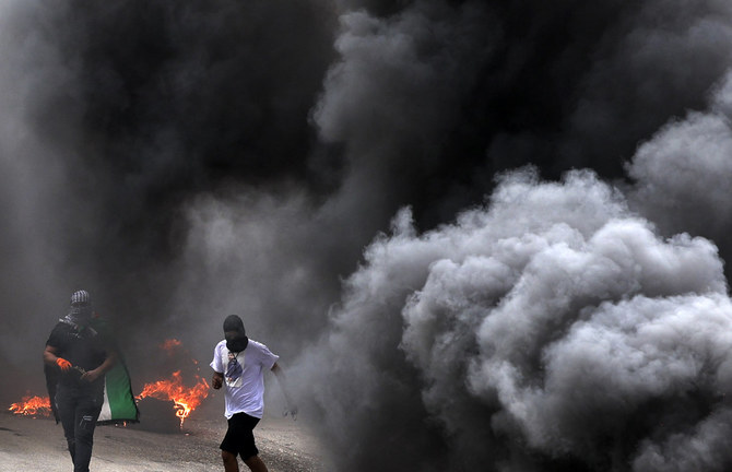 Palestinian protesters take cover behind smoke during clashes with Israeli forces in the village of Burqa, in the occupied West Bank, on April 19, 2022. (JAAFAR ASHTIYEH / AFP)