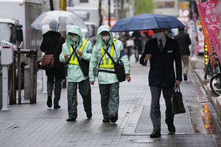 Parking enforcement workers wearing face masks walk on a street looking for parking violation in Tokyo, Friday, April 15, 2022. (AP)