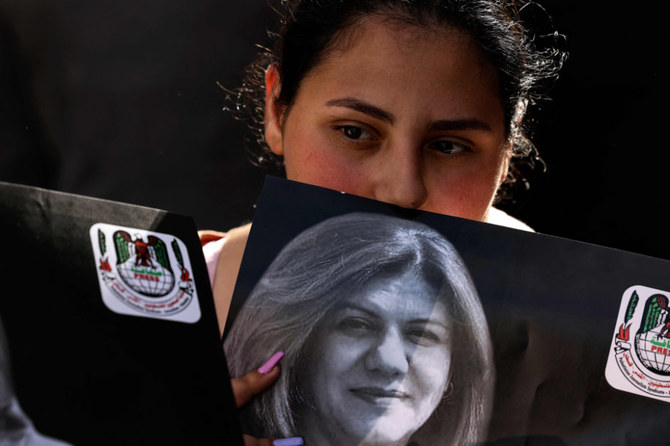 A Palestinian woman holds a photograph of slain veteran Al-Jazeera journalist Shireen Abu Akleh, as her body is carried toward the offices of the news channel in the West Bank city of Ramallah, on May 11, 2022. (AFP)