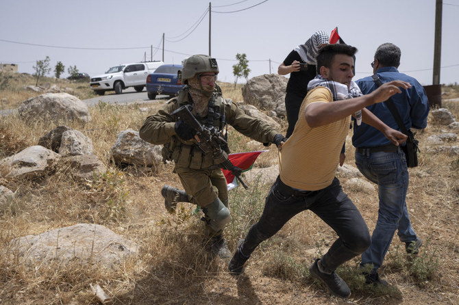 An Israeli soldier chases a protester while Palestinian and Israeli peace activists attempt to open a road to the Jewish settlement of Mezbi Yair, West Bank, on May 13, 2022. (AP Photo/Nasser Nasser)