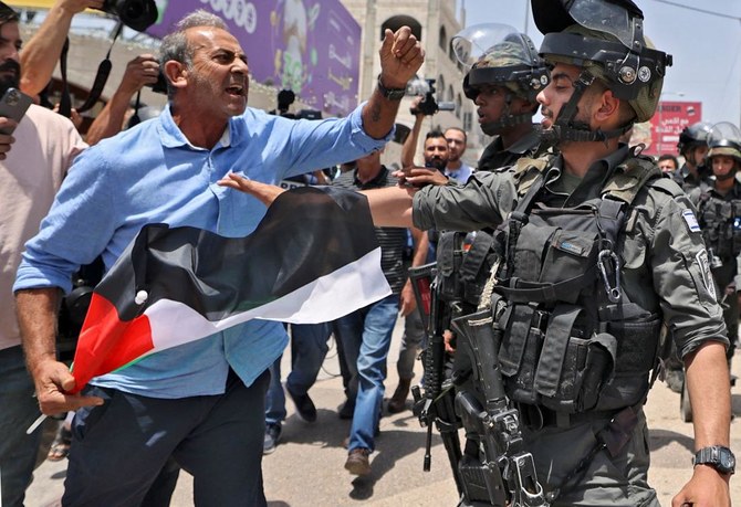 A Palestian man holding a national flag scuffles with Israeli border guards in the occupied West Bank town of Hauwara, on Friday. (AFP)