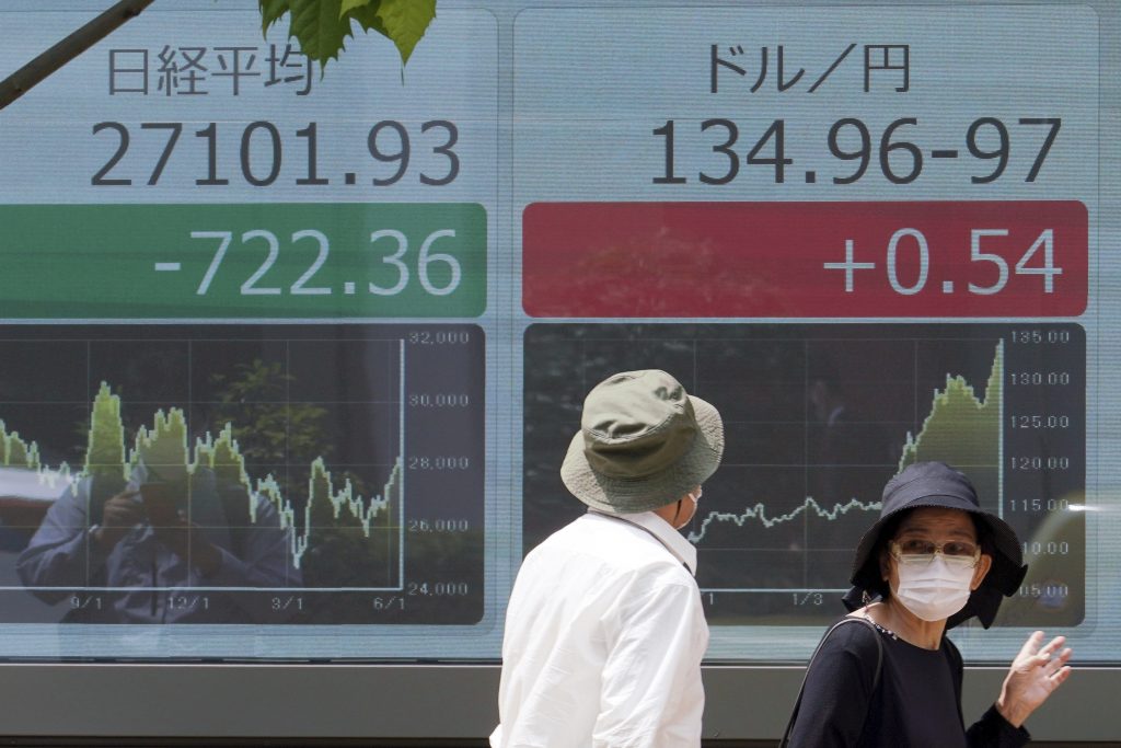 A woman and a man wearing protective masks walk in front of an electronic stock board showing Japan's Nikkei 225 index and U.S. dollar/Japanese yen exchange rate at a securities firm, June 13, 2022, in Tokyo. (File photo/AP)