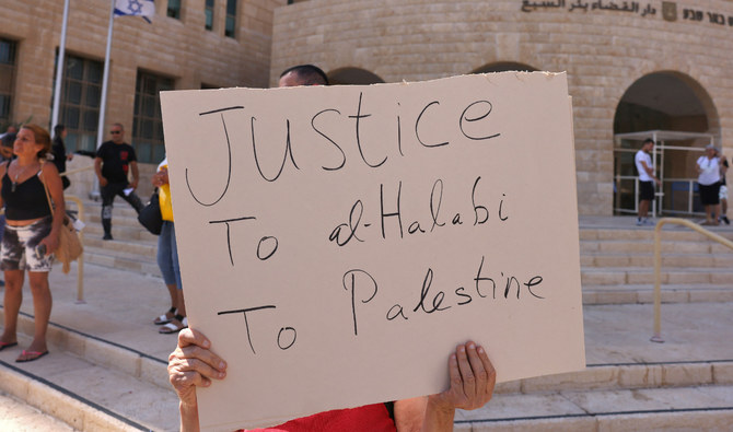A left-wing activist holds a placard outside an Israeli court during the trial of Palestinian Mohammed Halabi, the Gaza director of World Vision, a major US-based Christian NGO, in Beersheva on June 15, 2022. (AFP)