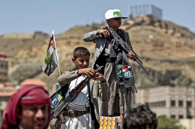 A boy lines up a round of ammunition atop the barrel of an assault rifle, with a flag sticking from his jacket showing a picture of a Houthi leader. (File/AFP)