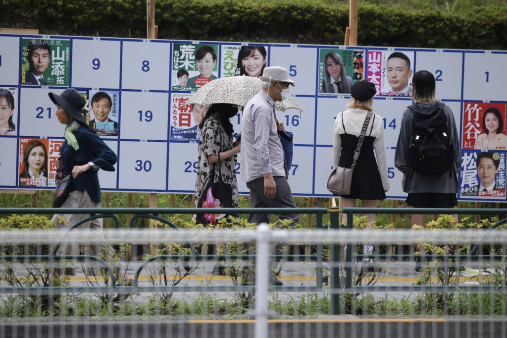Japanese people passing by look at a panel of  posters of candidates running for the the House of Councilors election.
