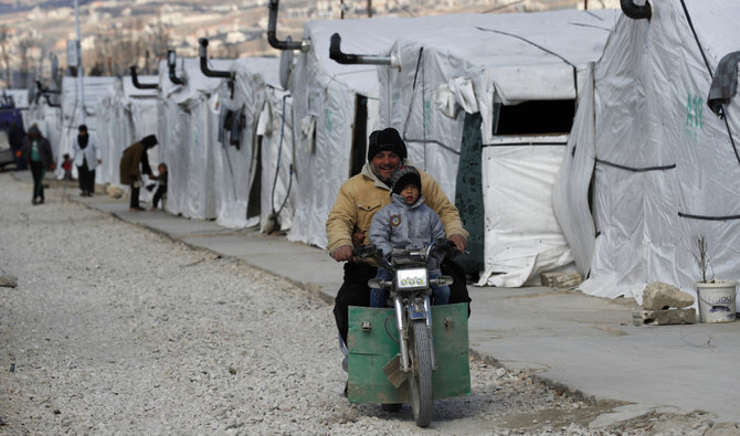 A Syrian displaced man and his son ride a motorcycle, as they drive between the tents at a refugee camp, in Bar Elias, in eastern Lebanon's Bekaa valley, March 5, 2021. (AP/File)