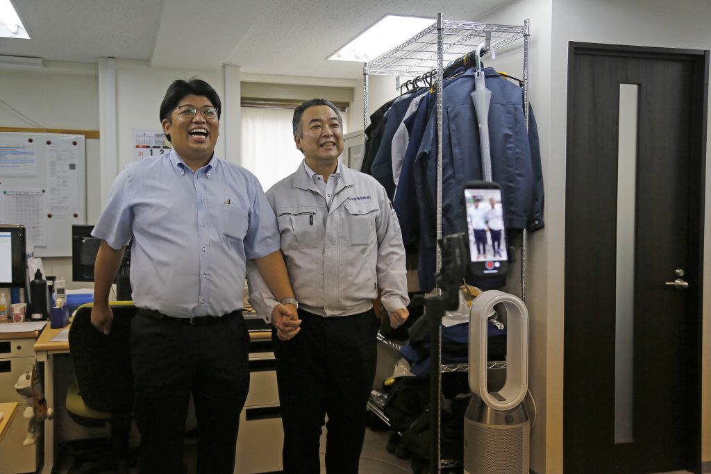Daikyo Security Chief Executive Daisuke Sakurai, left, and General Manager Tomohiko Kojima take a Tik Tok video together as seen on the screen in the device (right) at the Tokyo headquarters office of Daikyo Security Co. in Tokyo, Aug. 22, 2022. (File photo/AP)