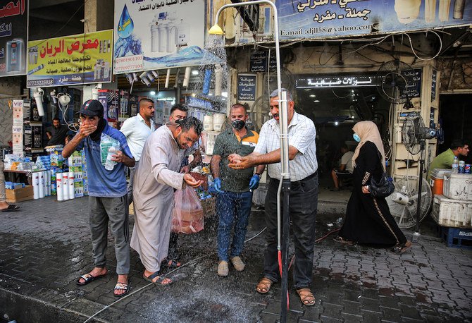 Men stand underneath a roadside shower along Sinak street in Baghdad to cool off due to extremely high temperature rises amid a heatwave. (AFP)