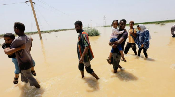 People cross the water during a flood in Al-Managil locality in Gezira state, Sudan, August 23, 2022. (Reuters)