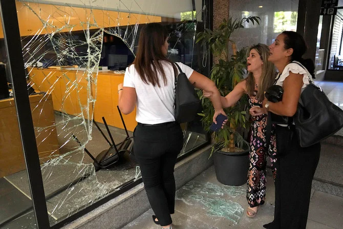 Panicked bank employees stand next to a window that was broken by attackers to exit the bank, in Beirut, Lebanon on Sept. 14, 2022. (AP)