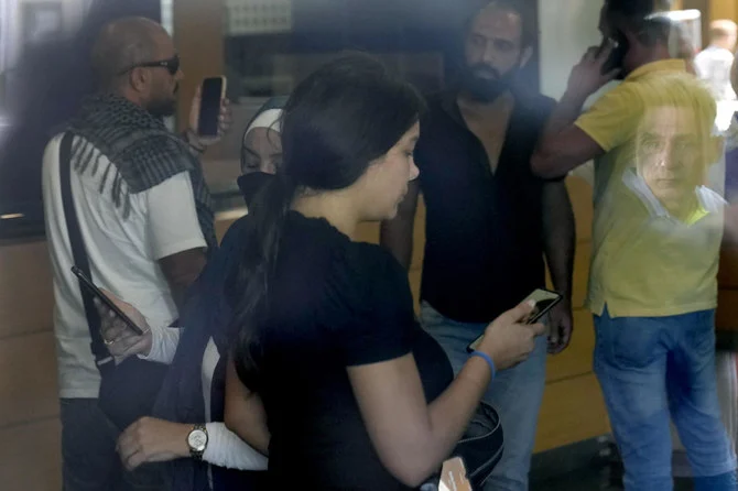 A man’s face is reflected on a window as Lebanese Sali Hafez, accompanied by activists, looks at her phone after breaking into a BLOM Bank branch brandishing a toy pistol and taking $13,000 from her trapped savings, in Beirut, on Wednesday. (AP)