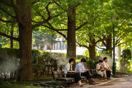 People rest on benches next to sprinklers on a hot day in Tokyo's Chuo district on September 14, 2022. (AFP)