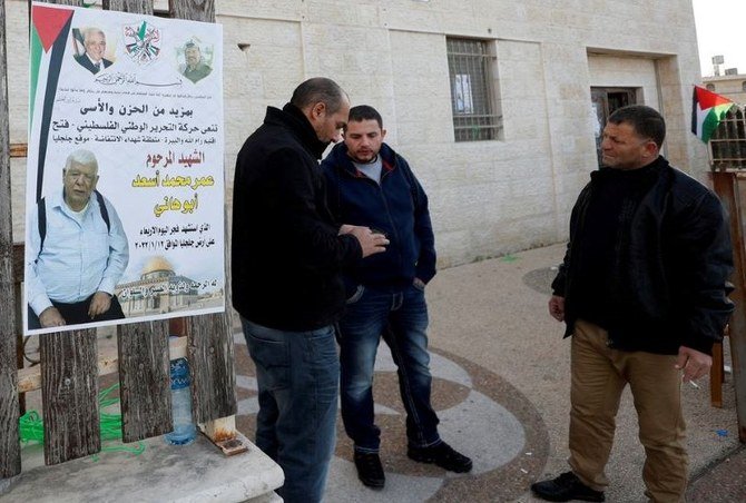 Men stand next to a poster of Palestinian-American Omar Abdalmajeed As’ad in Jiljilya village, Israeli-occupied West Bank, Jan. 12, 2022. (Reuters)
