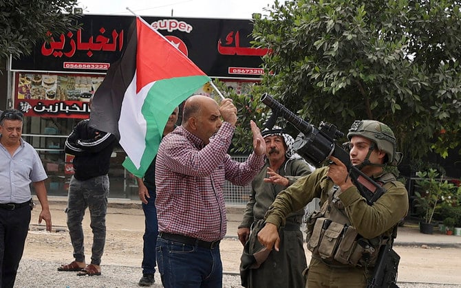 A protester waving a Palestinian flag argues with an Israeli soldier holding a tear gas launcher during clashes in the occupied West Bank. (File/AFP)