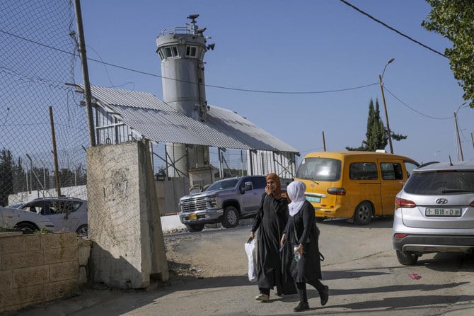 Palestinians walk past an Israeli military guard tower with two robotic guns and surveillance cameras at the Aroub refugee camp in the West Bank, Thursday, Oct. 6, 2022. (AP Photo/Mahmoud Illean)