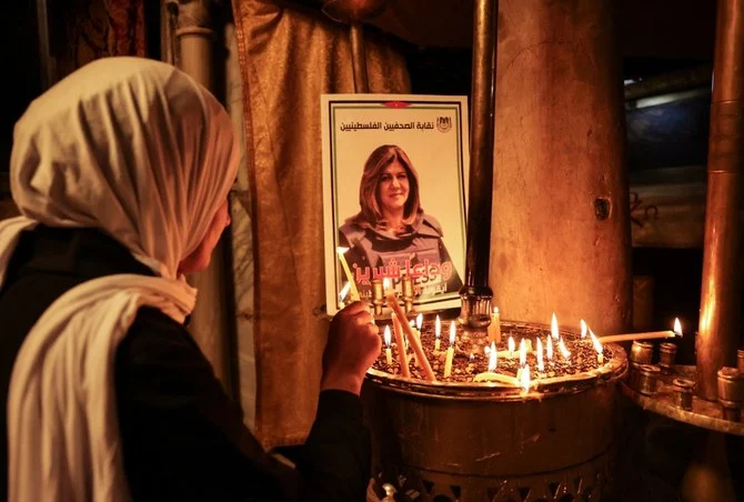 A woman lights a candle in front of a poster of slain journalist Shireen Abu Akleh (File/AFP)