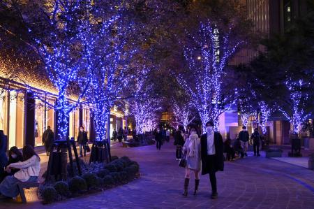 People walk along trees covered with decorative lights set up in the run-up to the Christmas season in downtown Tokyo on November 18, 2022. (Photo by Richard A. Brooks / AFP)