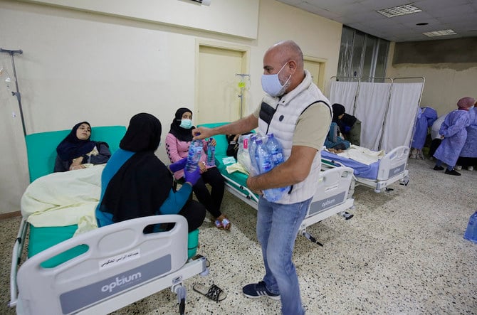 A man hands out water bottles to people waiting on patients infected in an outbreak of cholera, receiving treatment in north Lebanon. (File/AFP)