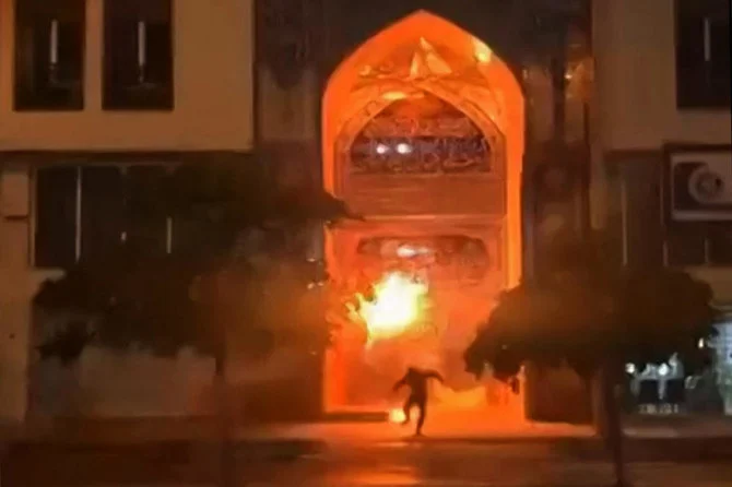 This image grab from a UGC video posted on December 11, 2022, reportedly shows a protester placing an object at the entrance of the Khomeini Seminary in Iran’s Bushehr city, before fleeing the scene as the object erupts in flames. (AFP)